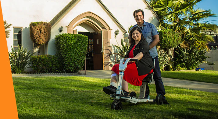 Couple smiling outdoors with woman seated on ATTO electric scooter in front of building.